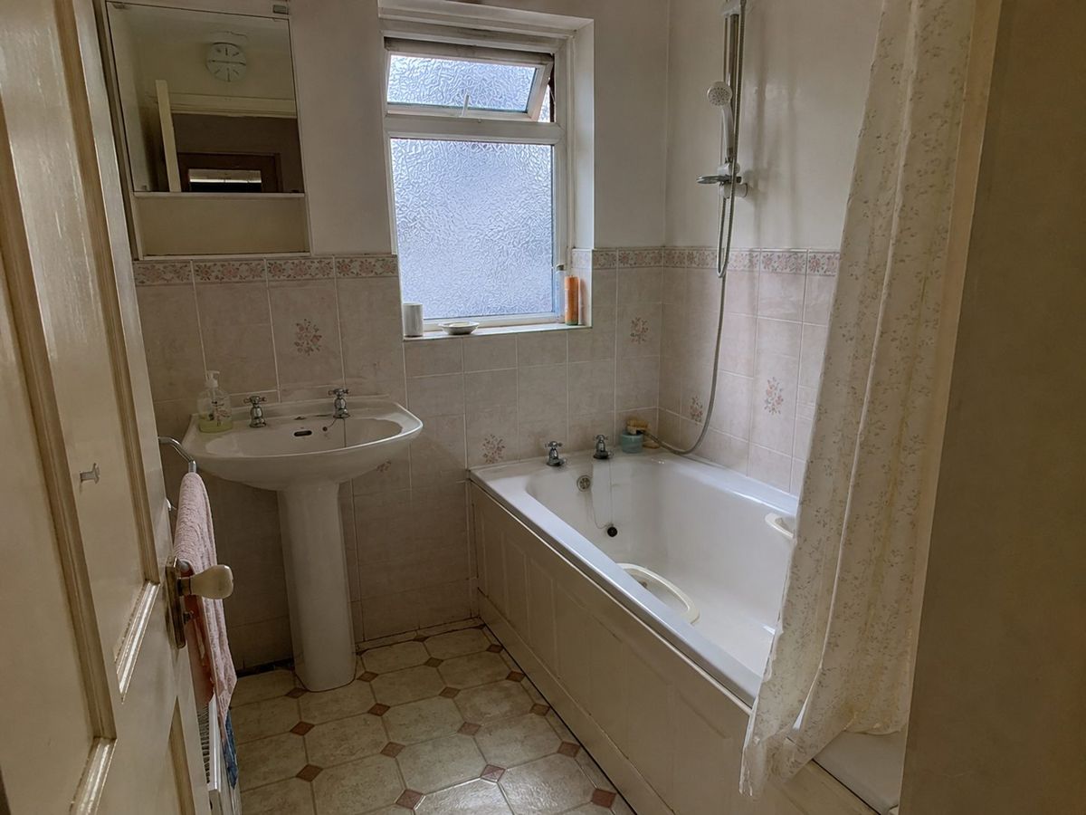 Before: a dated bathroom with a pedestal basin, bath and patterned tiles