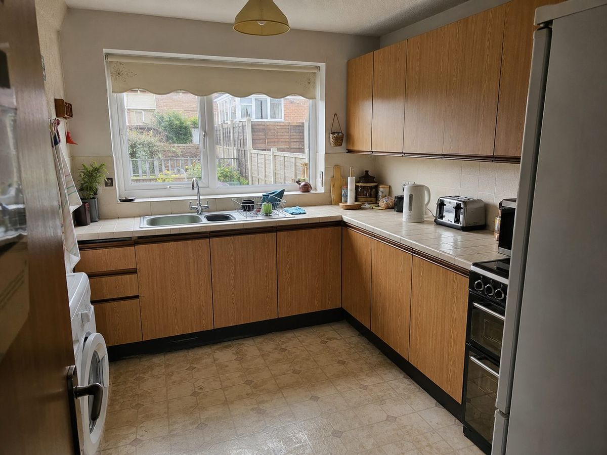 The original kitchen with dated wood-effect units, tiled worktop and worn vinyl floor