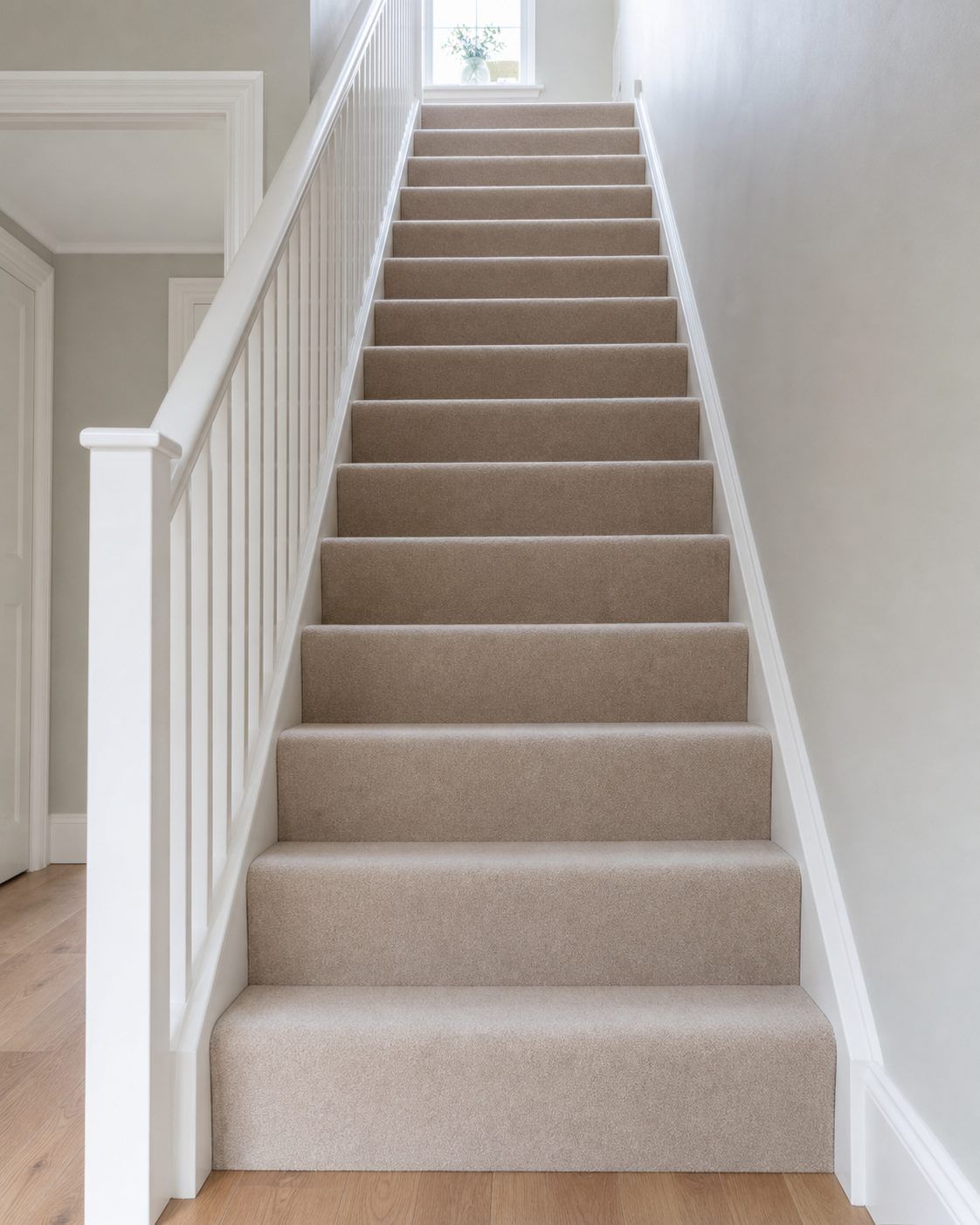 A staircase with a neutral stair carpet and white painted spindles