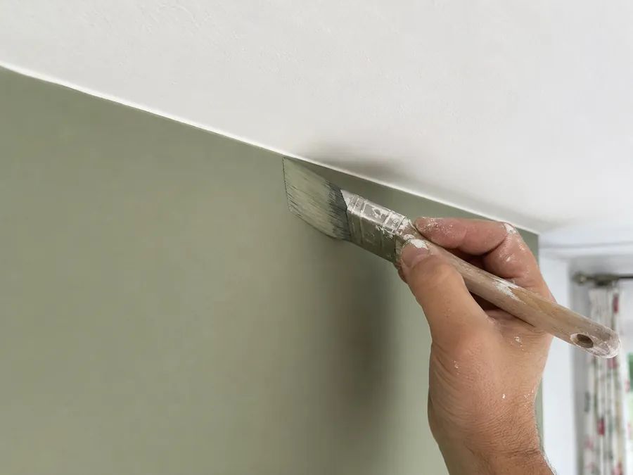 Sage green paint being cut in by hand along a ceiling line